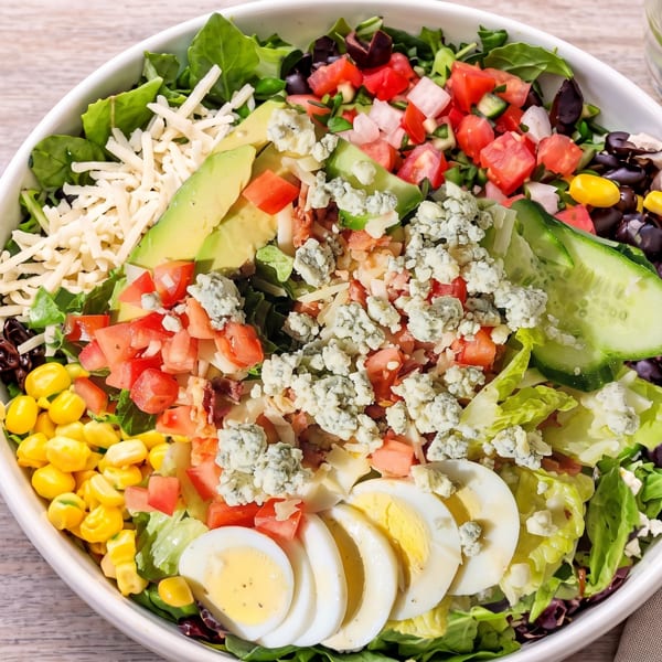 Overhead view of a vibrant Cobb salad with avocado, corn, tomatoes, eggs, and blue cheese.